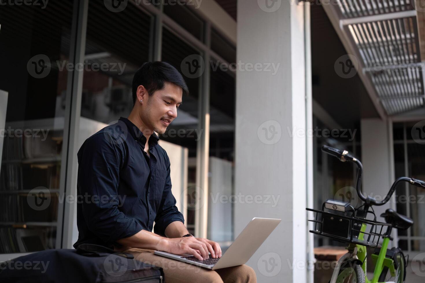 A young Asian businessman rides a bicycle to work. Use a reusable water bottle. Working outside of the office using a laptop The concept of saving energy and reducing pollution to the environment. photo