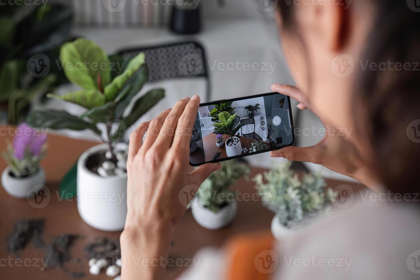A young Asian woman uses her phone to take photos and enjoys planting plants in her garden to create a pleasant atmosphere in the house.