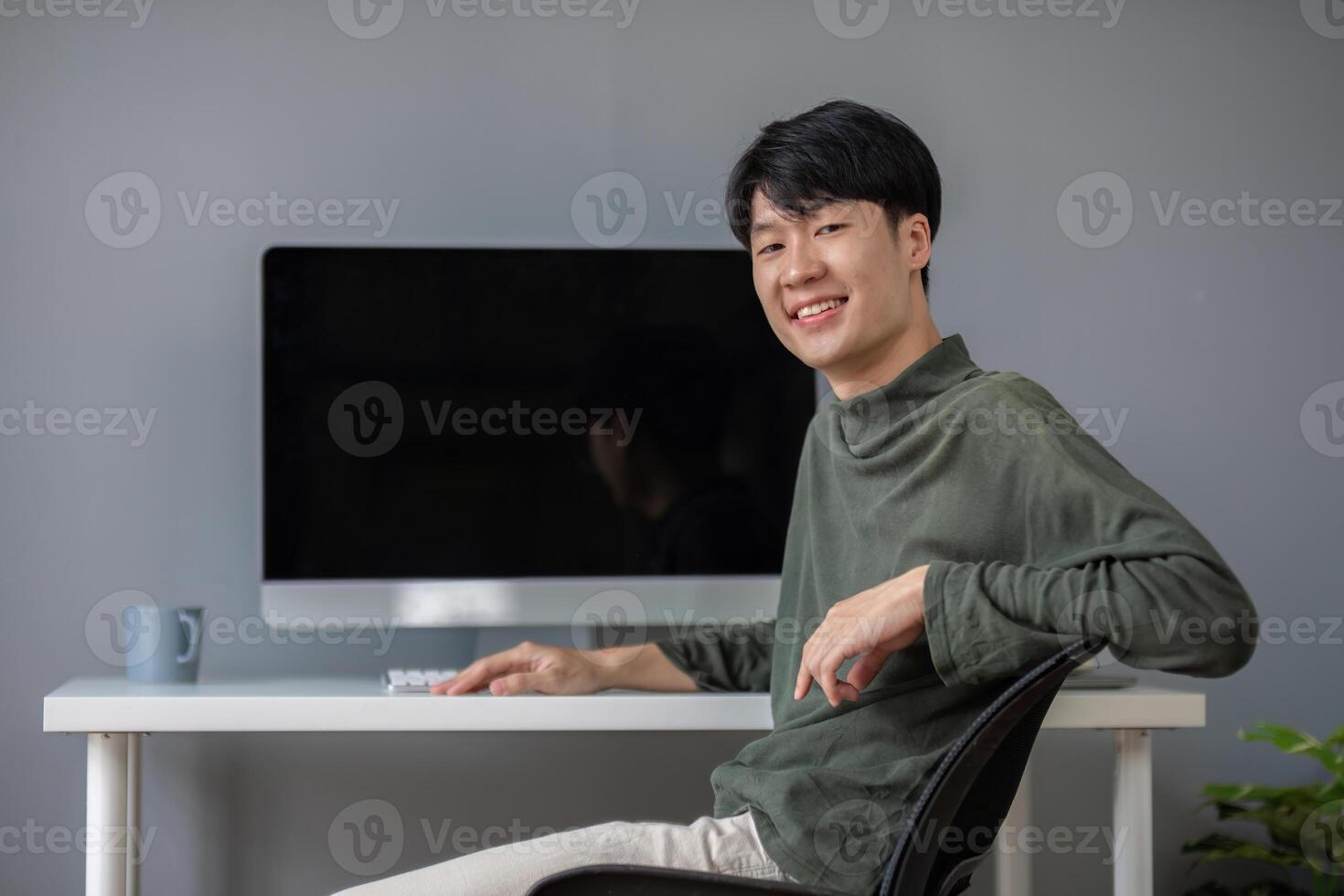 Young Asian student smiling happily at computer with blank screen on table photo