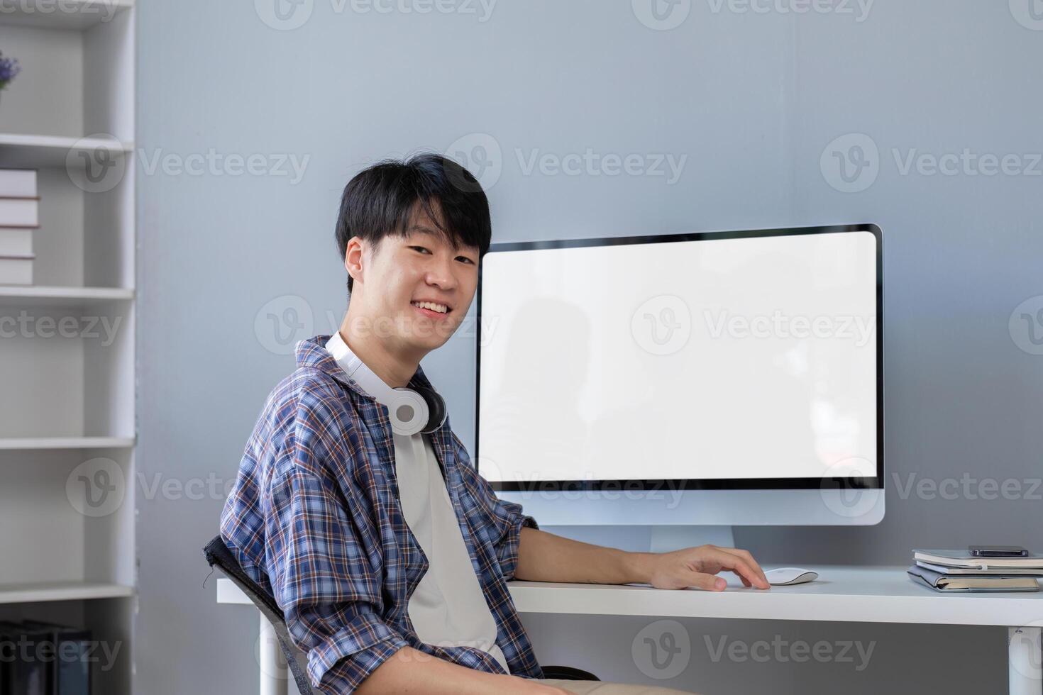 Young Asian student smiling happily at computer with blank screen on table photo