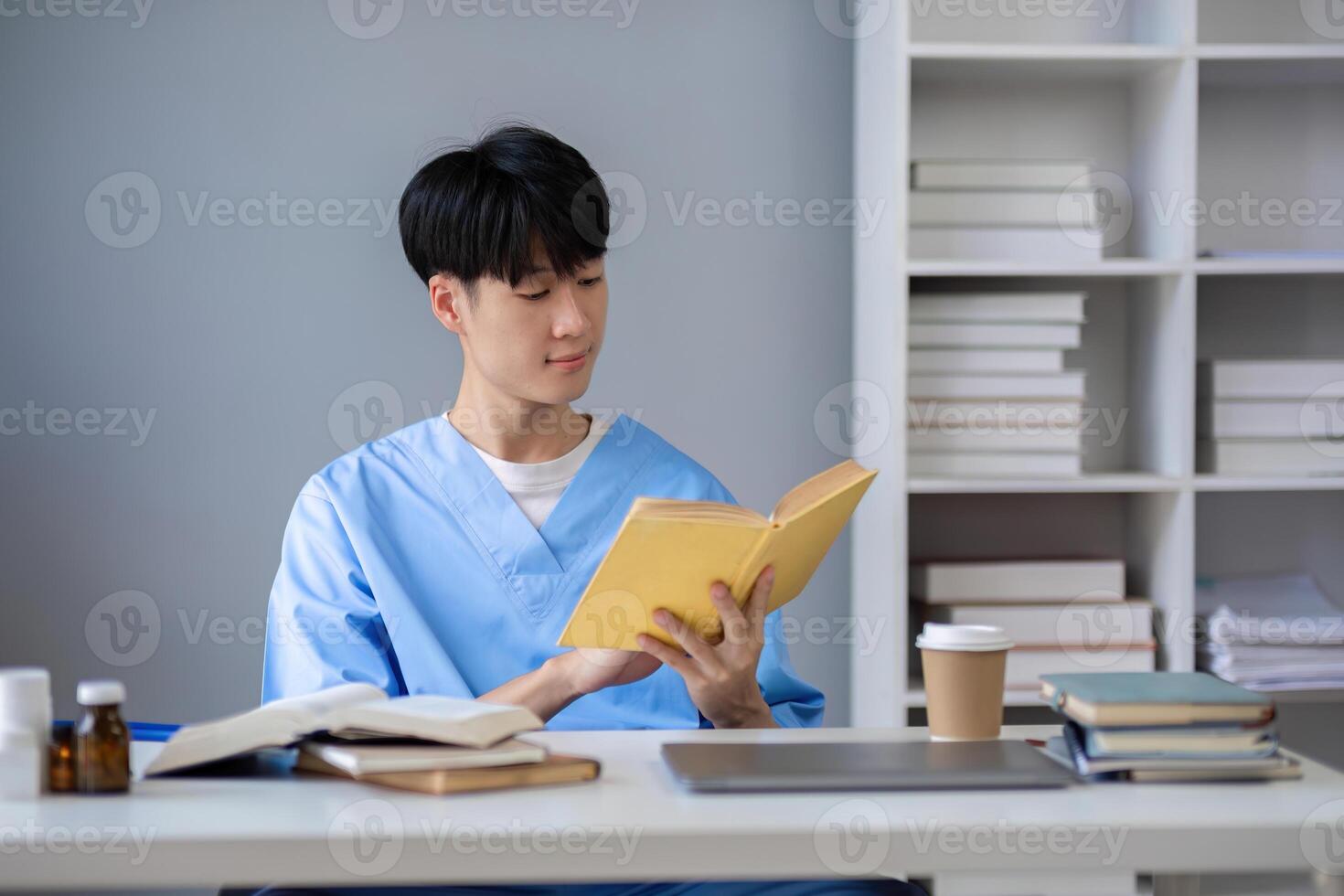 A male medical student sits and reads a book in the library to prepare for a research exam for a medical subject. photo