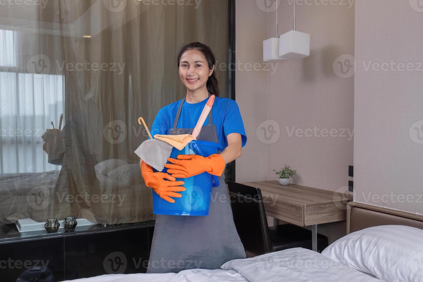The cleaning lady wears orange rubber gloves and carries a bucket of bedroom cleaning supplies. photo