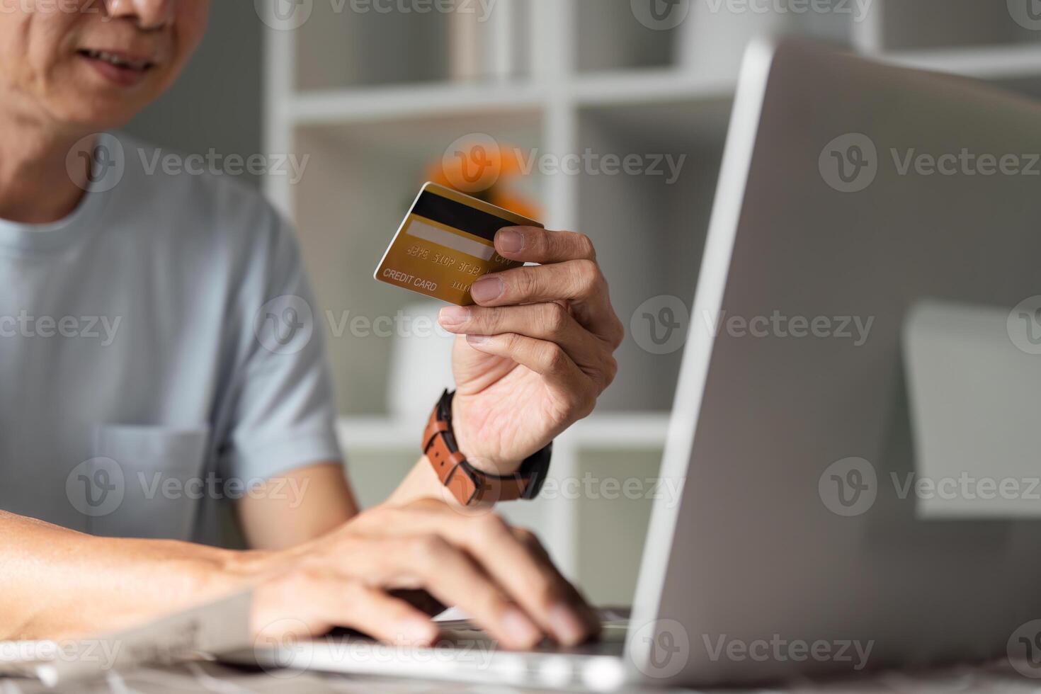 Close-up of a senior man with a credit card shopping online at home using a laptop photo