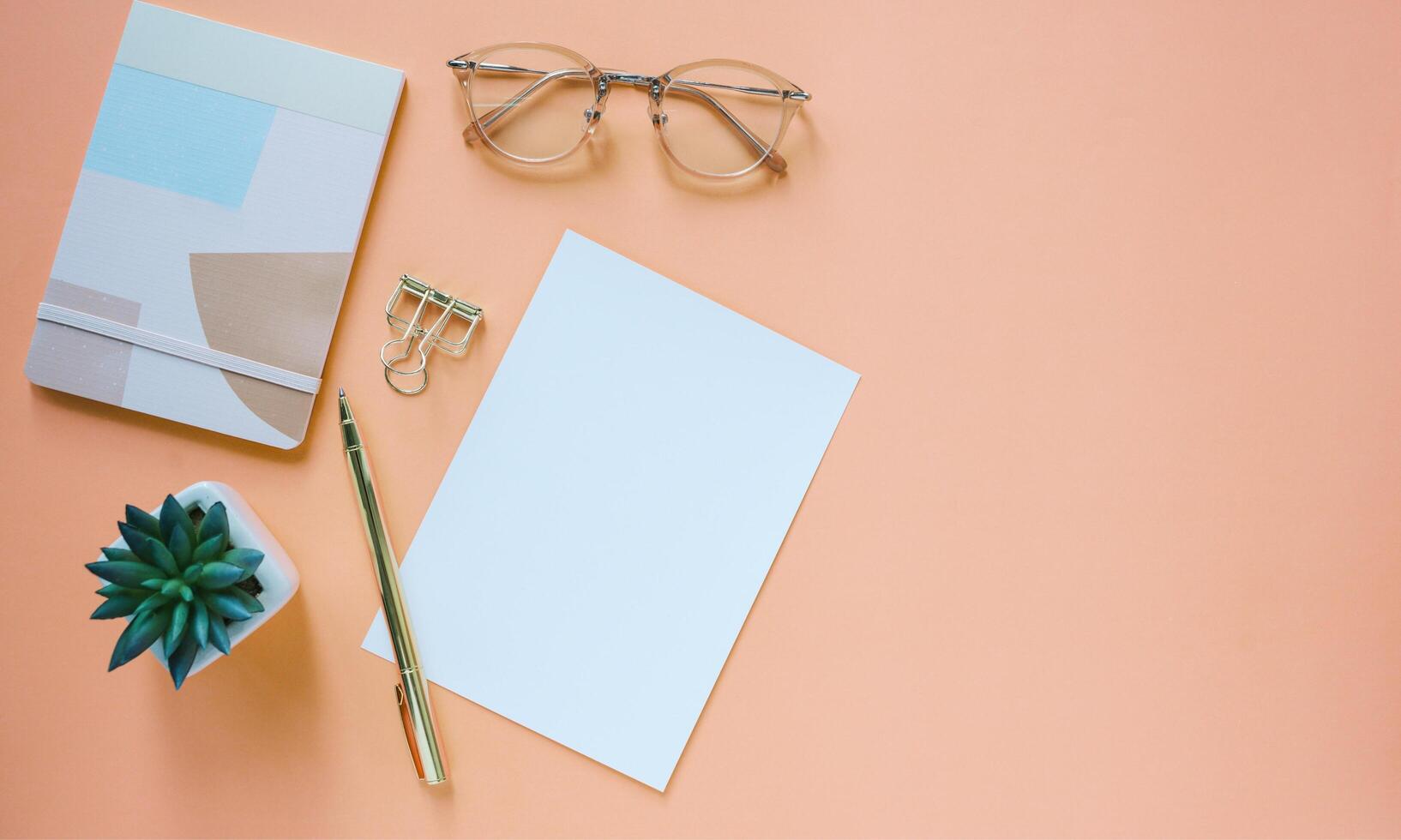 Blank paper, pen, glasses, and notebook on orange background photo