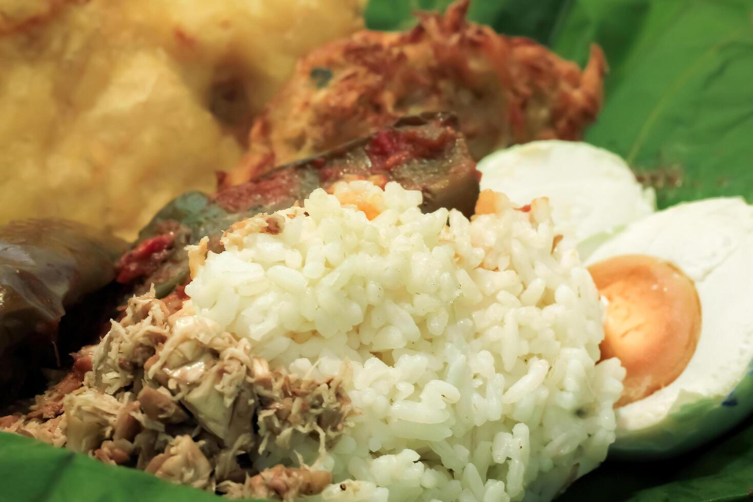 megono rice is traditional food from central java, Indonesia. megono rice with side dishes of salted egg, balado eggplant, bakwan and tempeh wrapped in teak leaves photo