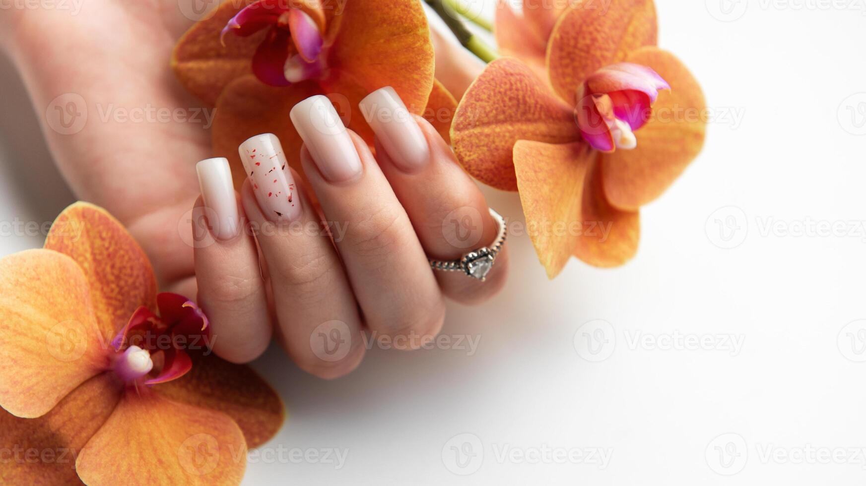 Woman hand showing stylish trendy nude manicure holding orange orchid flowers photo