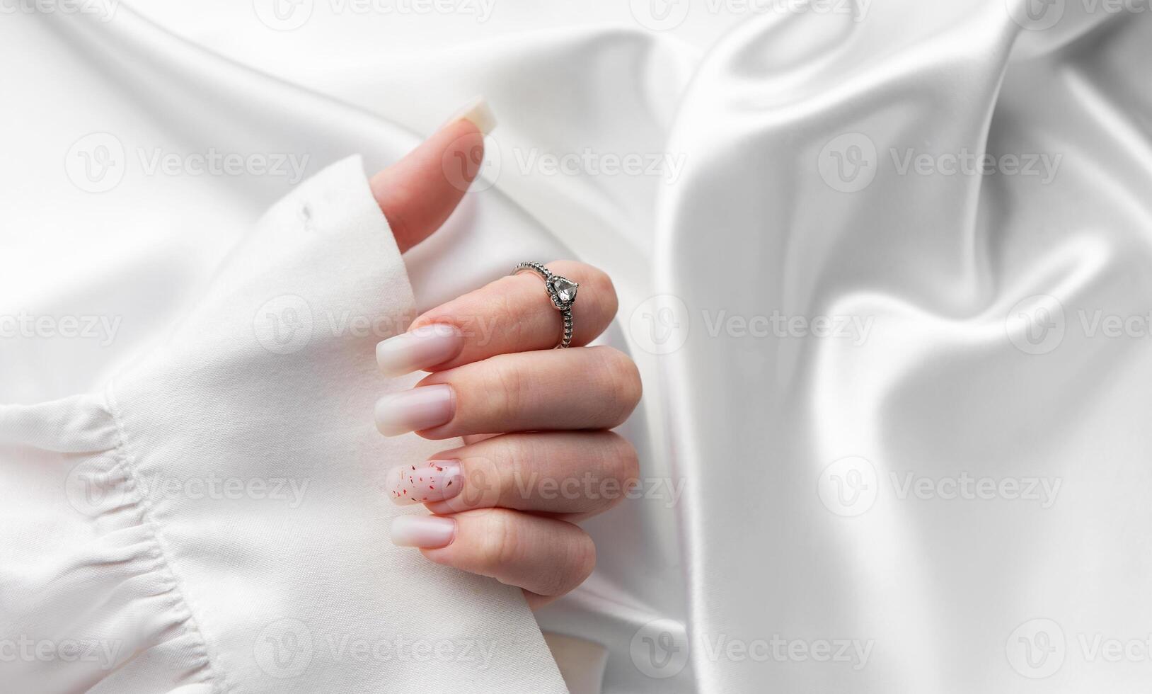 Woman stylish pastel pink manicure and silver ring on white silk fabric photo