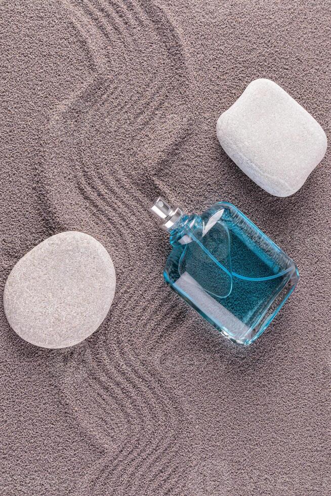 A blue bottle of men's cosmetics, spray, cologne, perfume lie on gray textured sand. oval stones. blank bottle mockup. A copy space. top vertical view photo