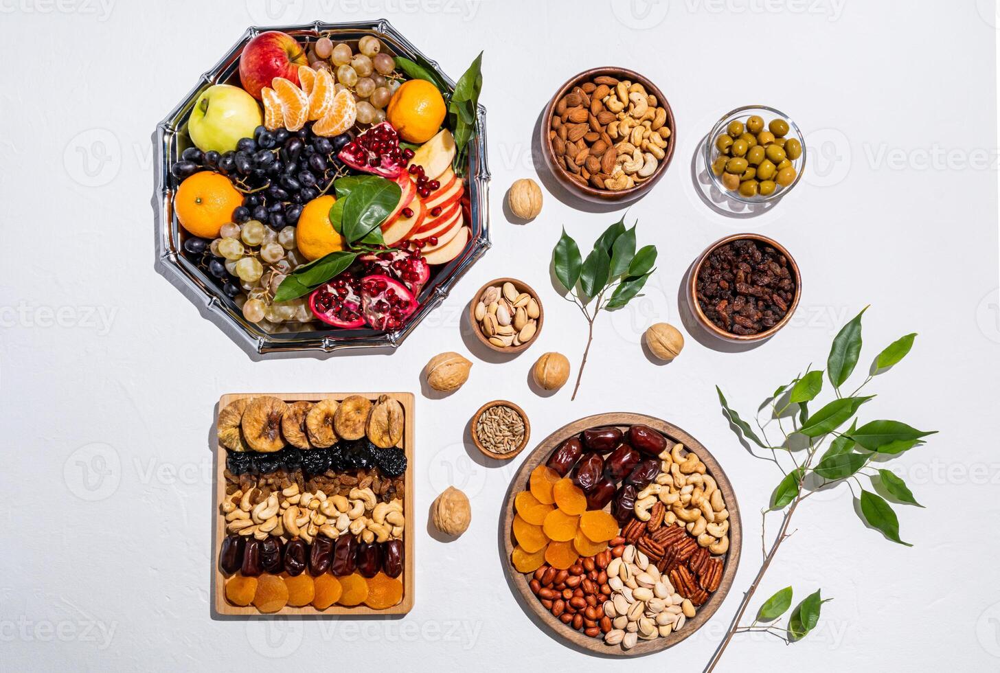 many different trays and bowls with traditional treats for the Tu Bi shvat. top view. white background. flat lay. green branches of the tree. photo
