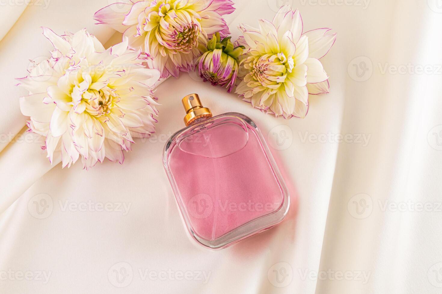 A chic bottle of women's perfume on a creamy satin background among the flowers of the dahlia. top view. blank bottle mockup. Fragrance presentation photo