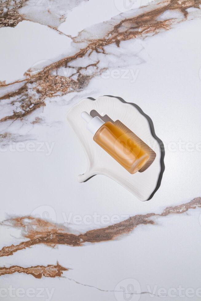 A chic cosmetic bottle with serum for daily self-care on a white tray in the form of a shell. top vertical view. Abstract marble. Natural Cosmetic. photo