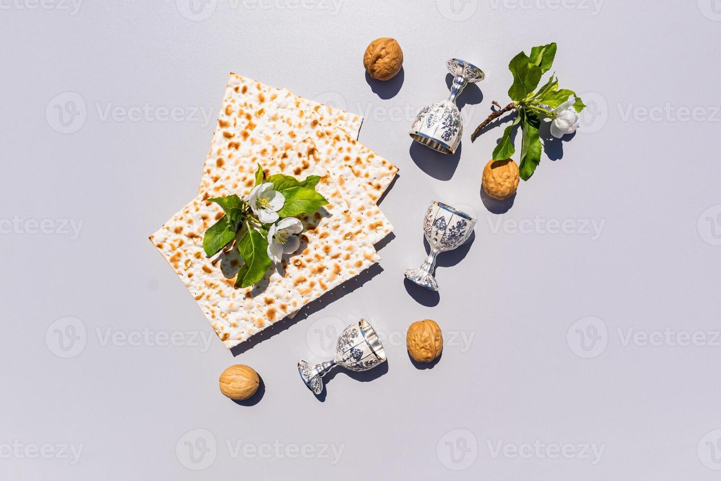 The concept of the holiday of the Jewish Passover. A slices of Easter matzah, walnuts, silver glasses on a gray background. top view. apple blossom. photo