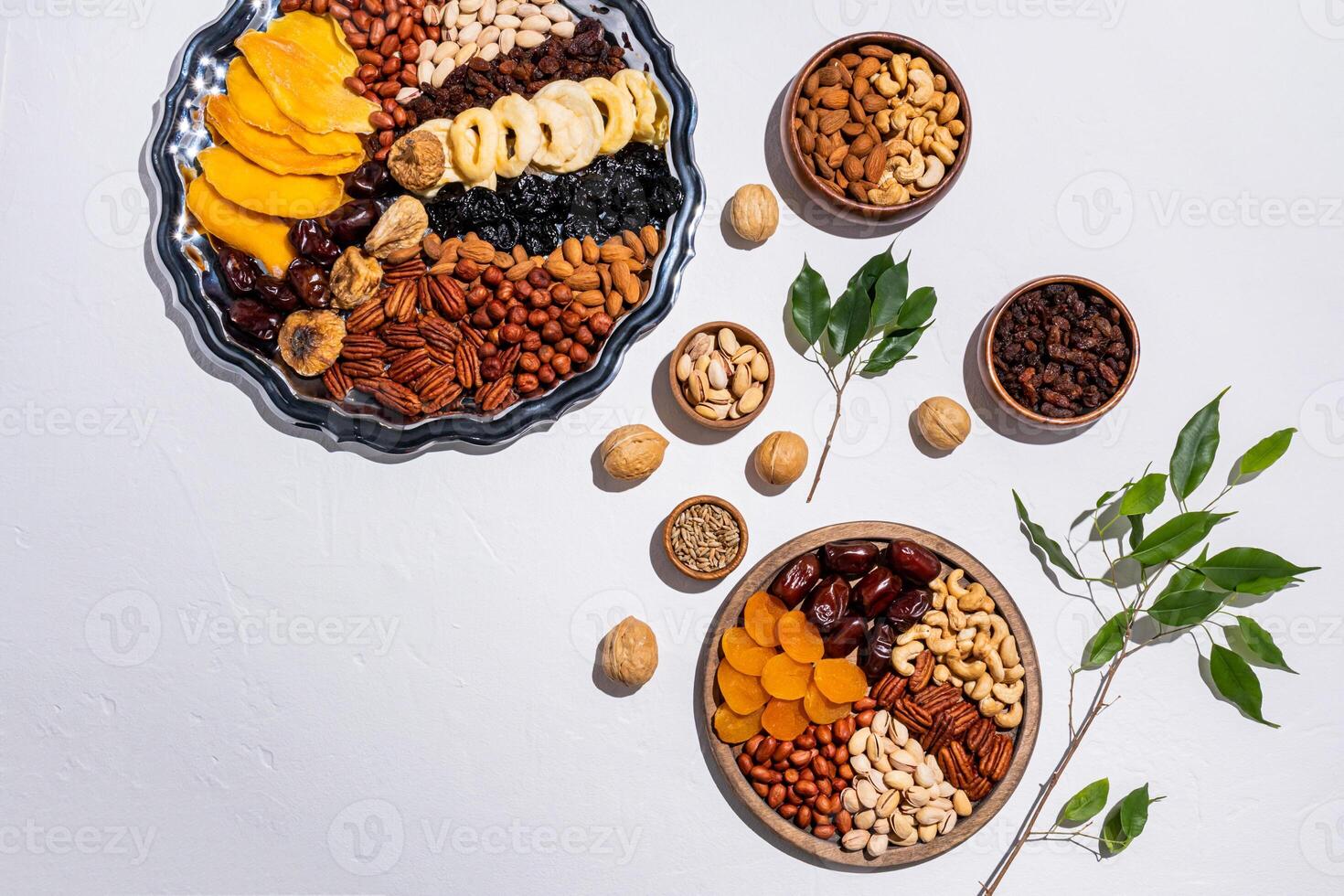 Two dishes with traditional dried fruit and nut treats for Tu Bi Shvat on a white background with a green tree branch. top view. Flat lay photo