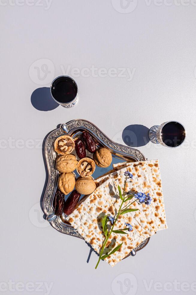matzoth on a silver tray with nuts, dates on a light background. glasses with red wine. A traditional treat for the Passover holiday. top view photo
