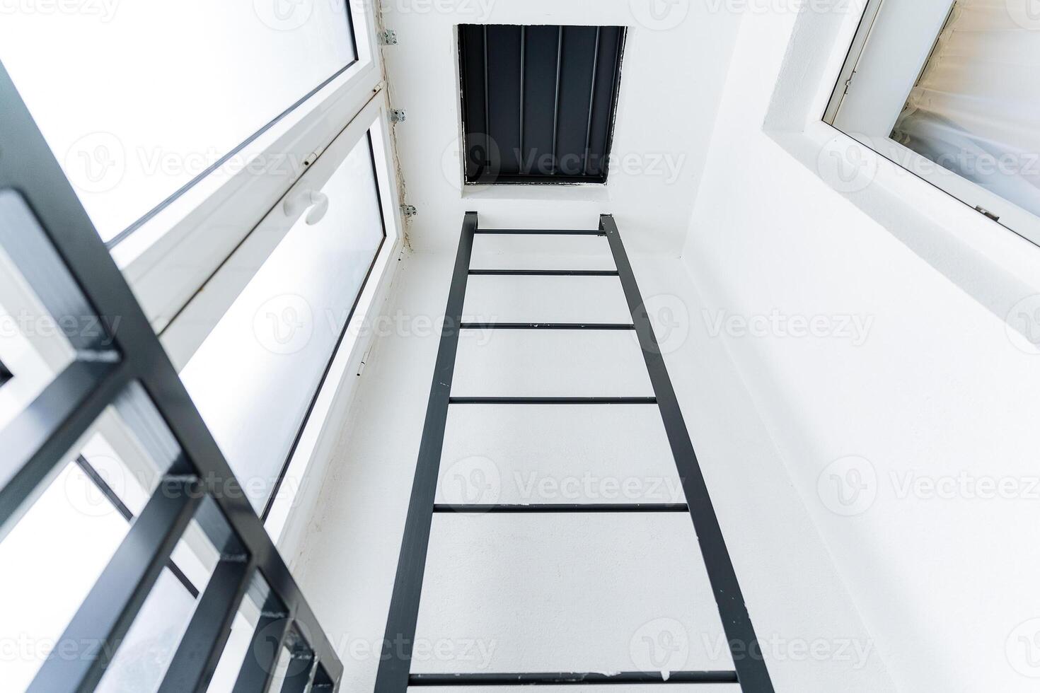 A ladder made of composite material going up against the parallel facade of a building with rectangular glass windows in a room. photo