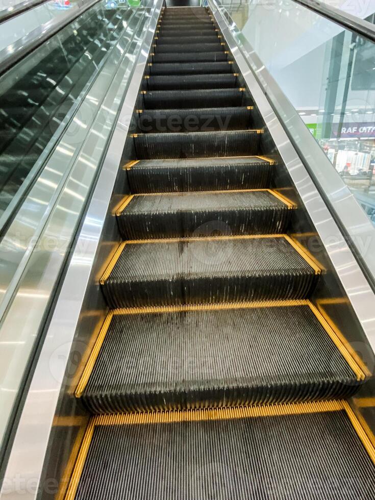 A wooden parallel rectangle building with a close-up yellow-lined escalator made of composite material, metal, glass, and track. photo