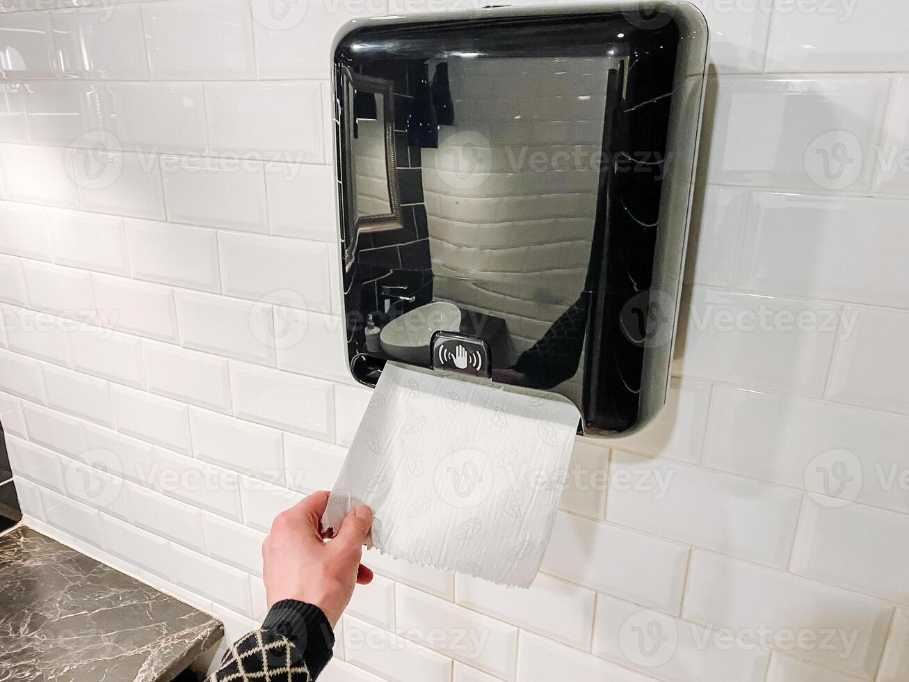 A person is operating a paper towel dispenser in a bathroom, inside a building. photo