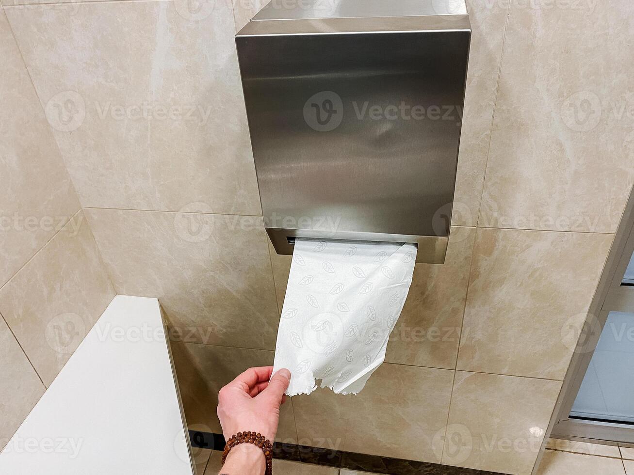 A person retrieving toilet paper from a stainless steel dispenser in a bathroom with hardwood flooring. photo
