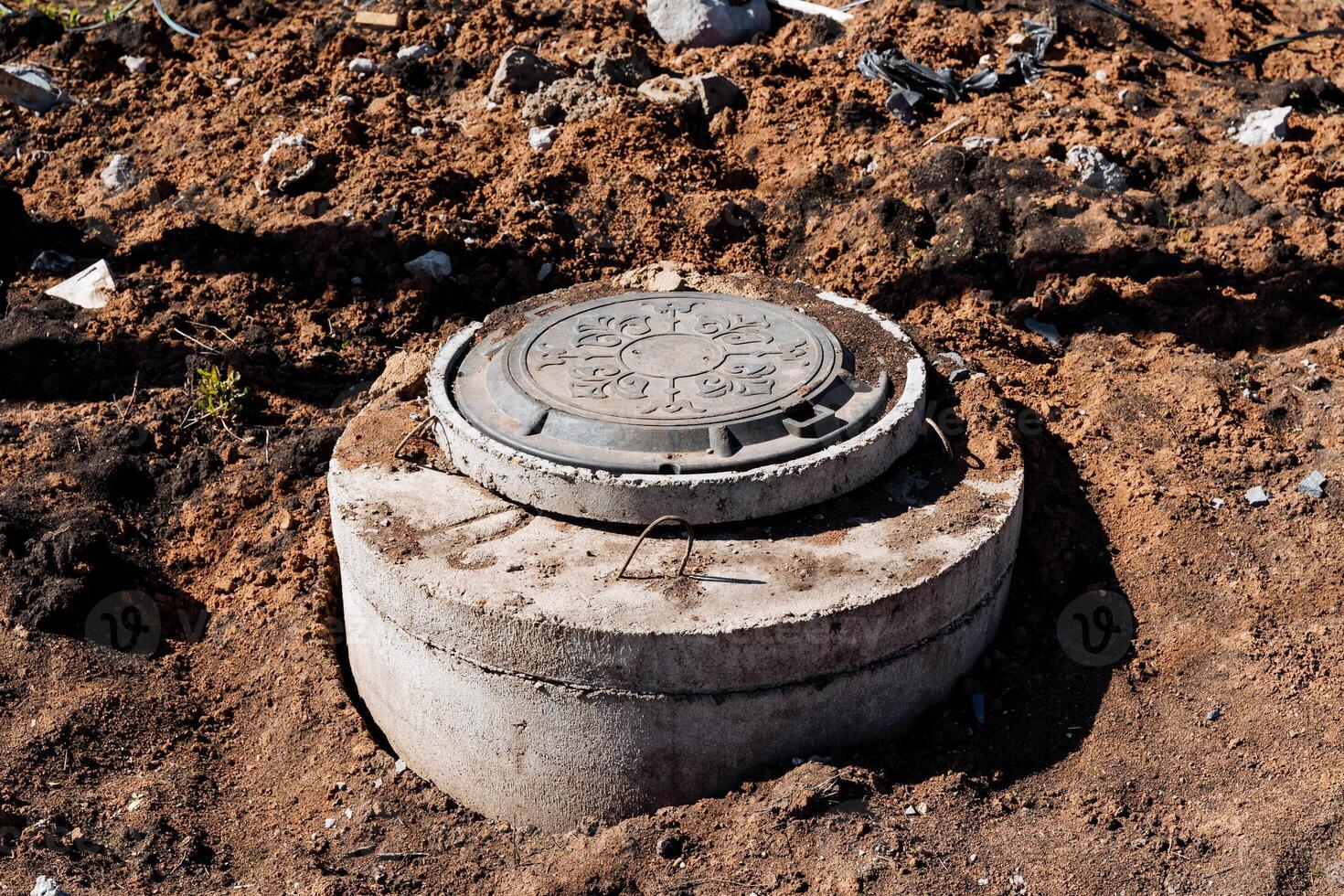 Closeup of a circular metal manhole cover on dirt ground at an urban construction site, showcasing essential infrastructure for sewer and sanitation services in the city photo