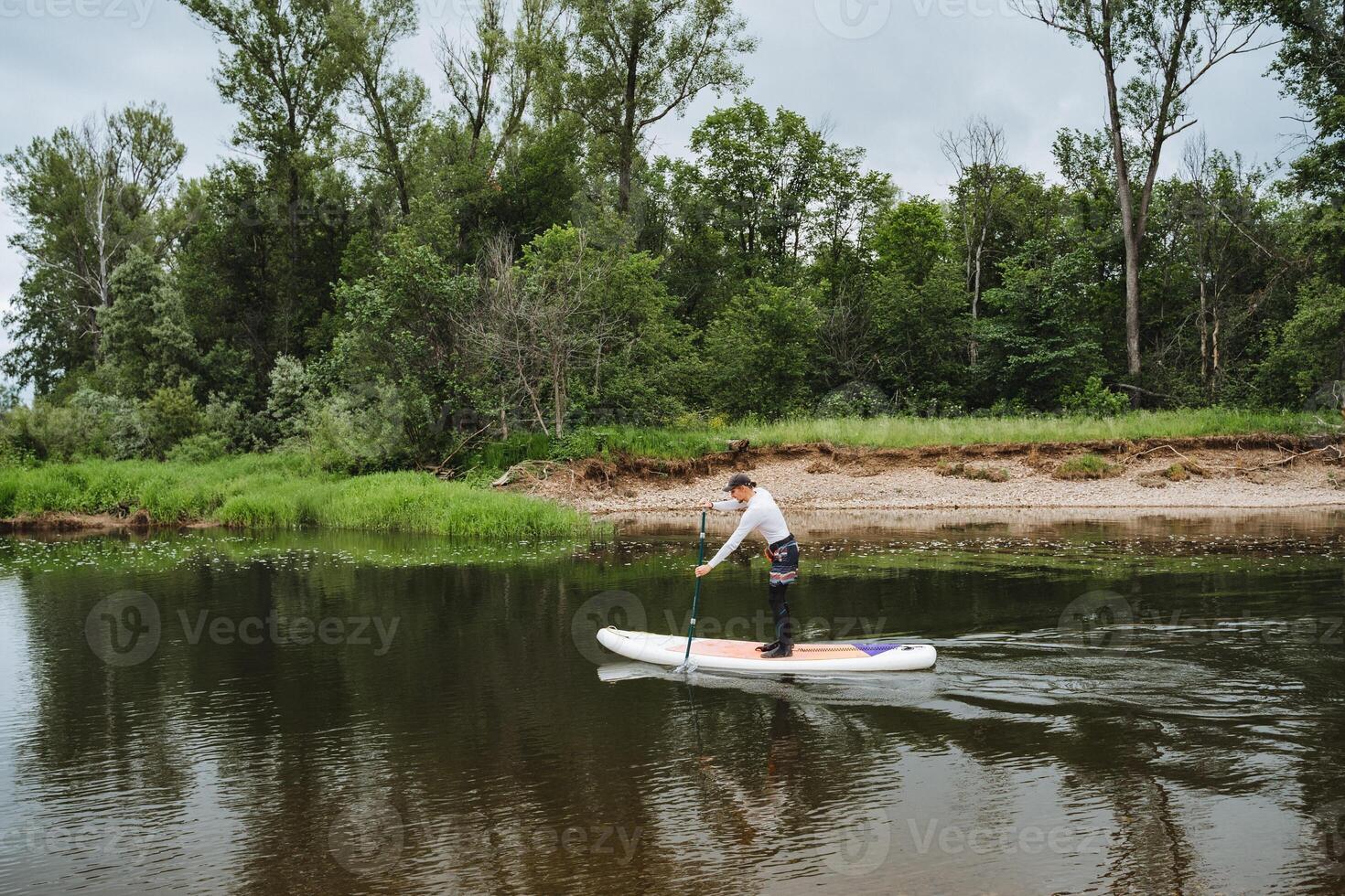 A man is enjoying paddleboarding on a tranquil river, surrounded by a lush forest, creating a mix of adventure and tranquility in stunning natural surroundings photo