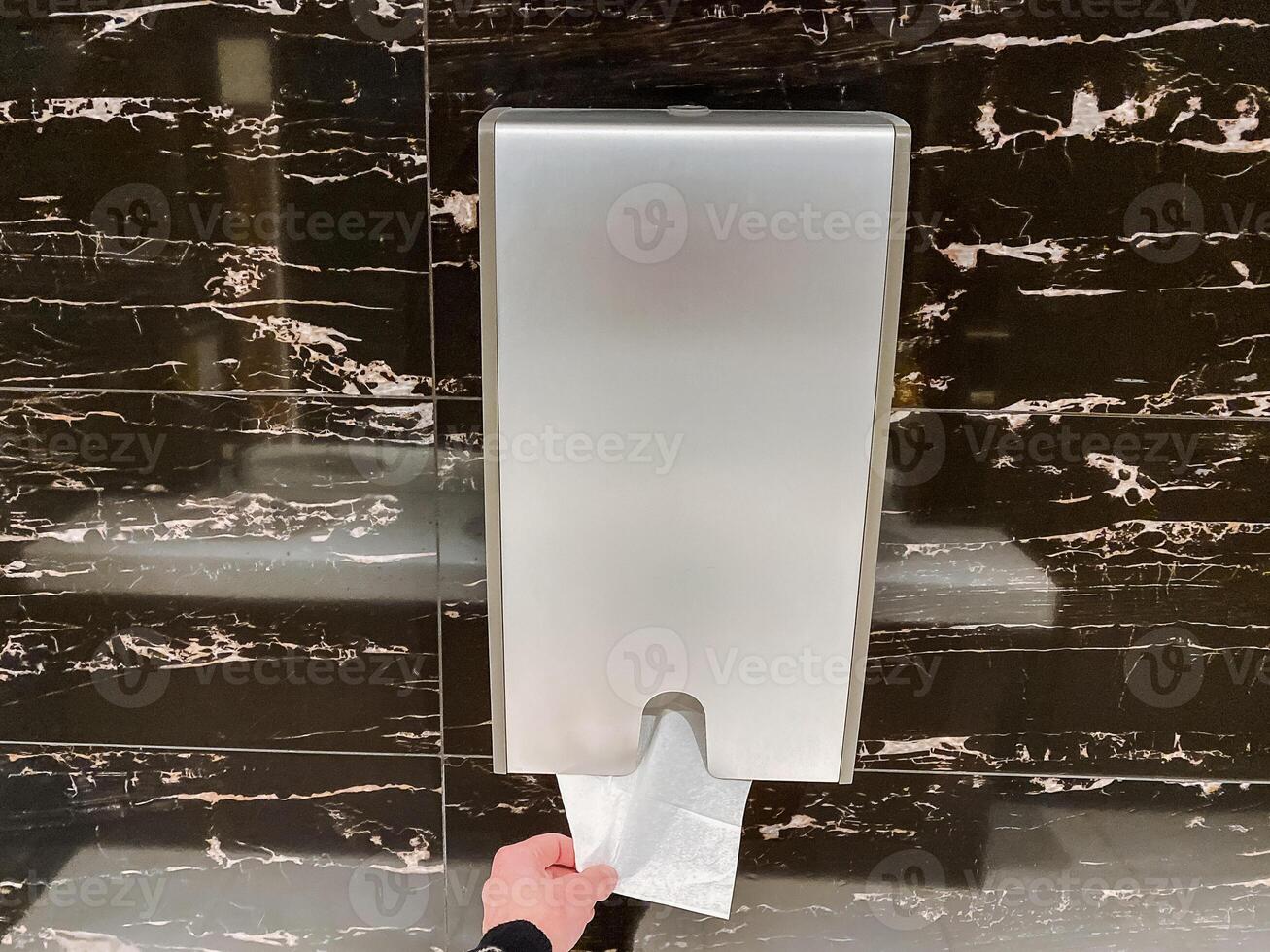 A person picks up a napkin from a dispenser filled with paper towels made of various materials like wood, metal, and composite. photo