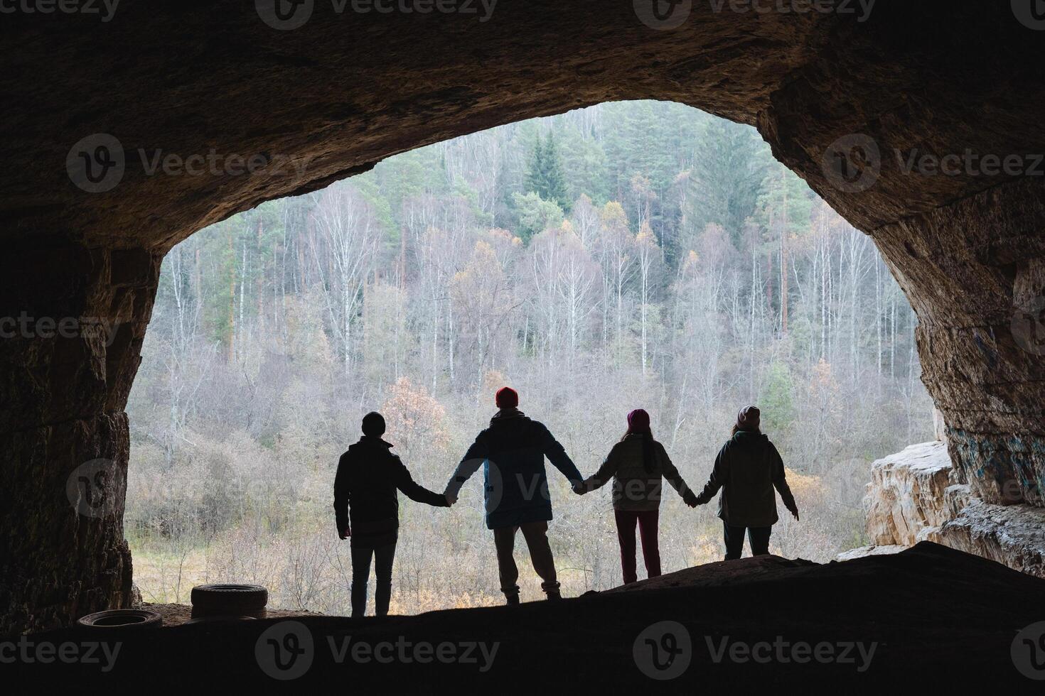 A group of individuals is standing together in a dimly lit cave, all holding hands in a circle, creating a sense of unity and togetherness amidst the stunning natural surroundings photo
