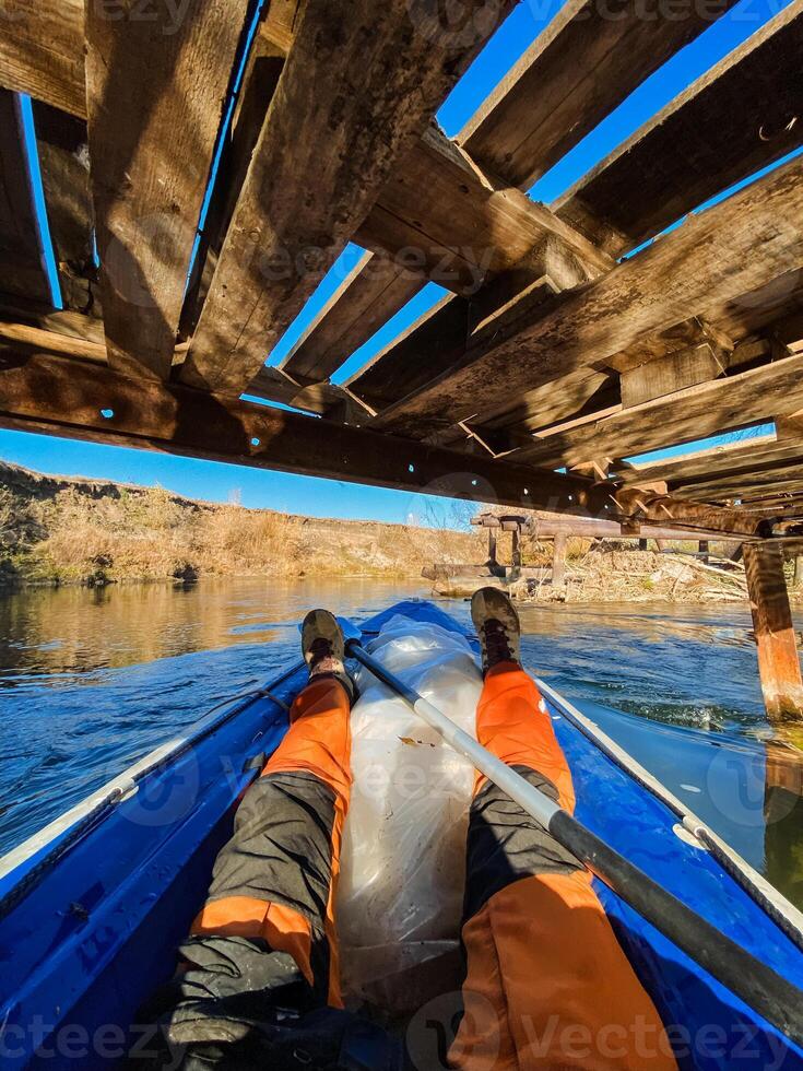 A person is paddling a blue kayak under a wooden bridge photo