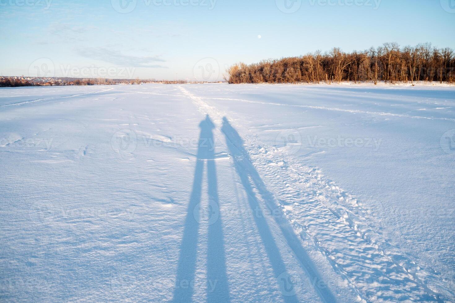 A persons shadow falls on the calm, freezing snowy field under the azure sky photo