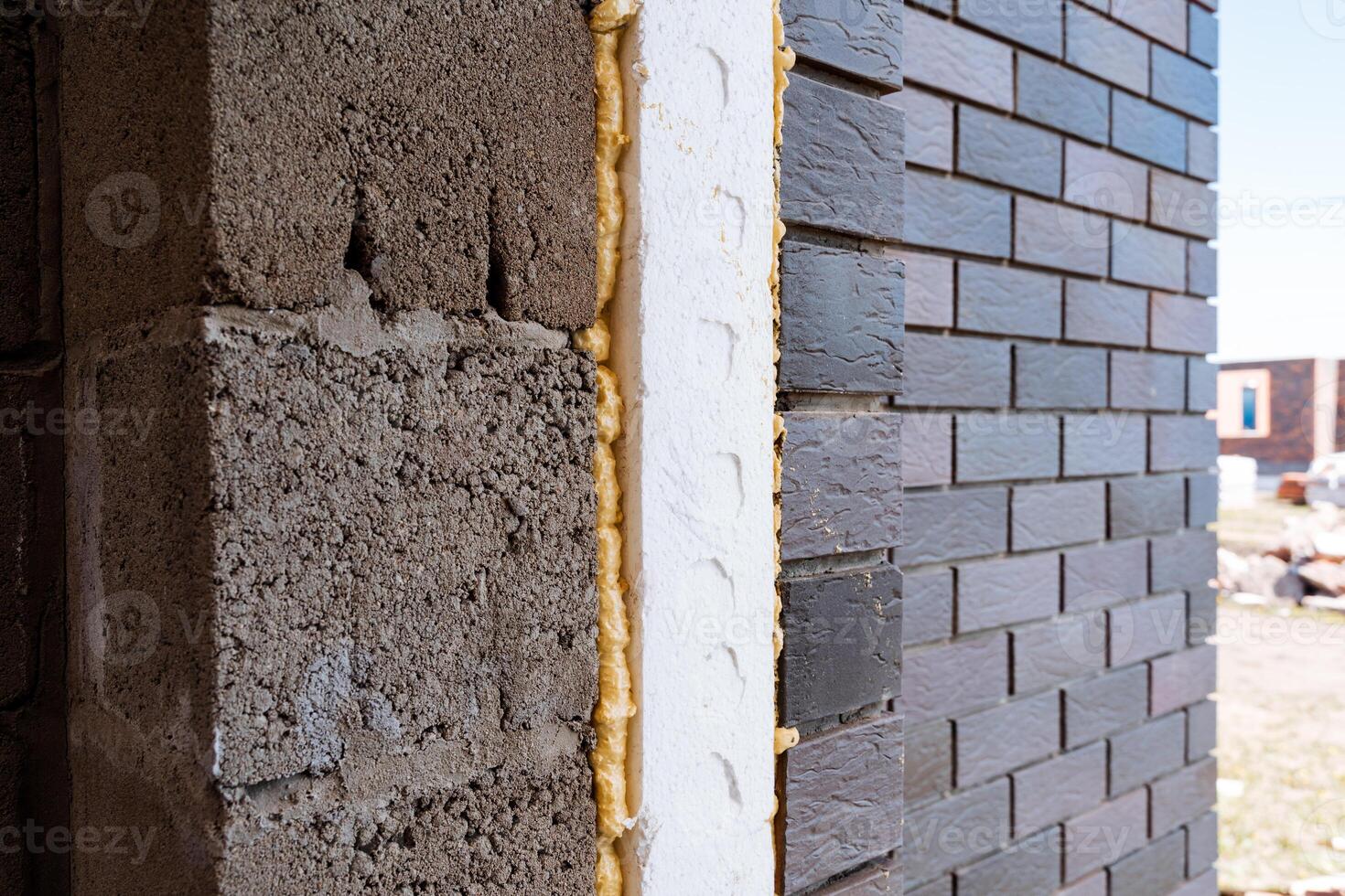 During construction, a building wall is being enhanced with insulating foam and brick to boost thermal efficiency and structural integrity, improving energy efficiency photo