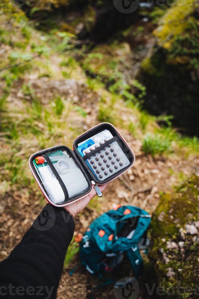 Hiker in forest holds open first aid kit, prepared for emergency with medical supplies and gear. Essential for safety in outdoor adventures and wilderness exploration photo