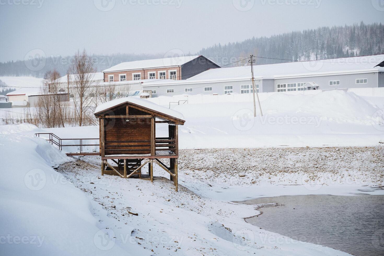 a small wooden house is sitting in the snow next to a body of water photo