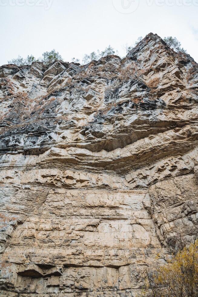 This image showcases a detailed close up of a rugged rocky cliff that towers prominently, with a magnificent mountain visible in the background, enhancing the overall scenic view photo