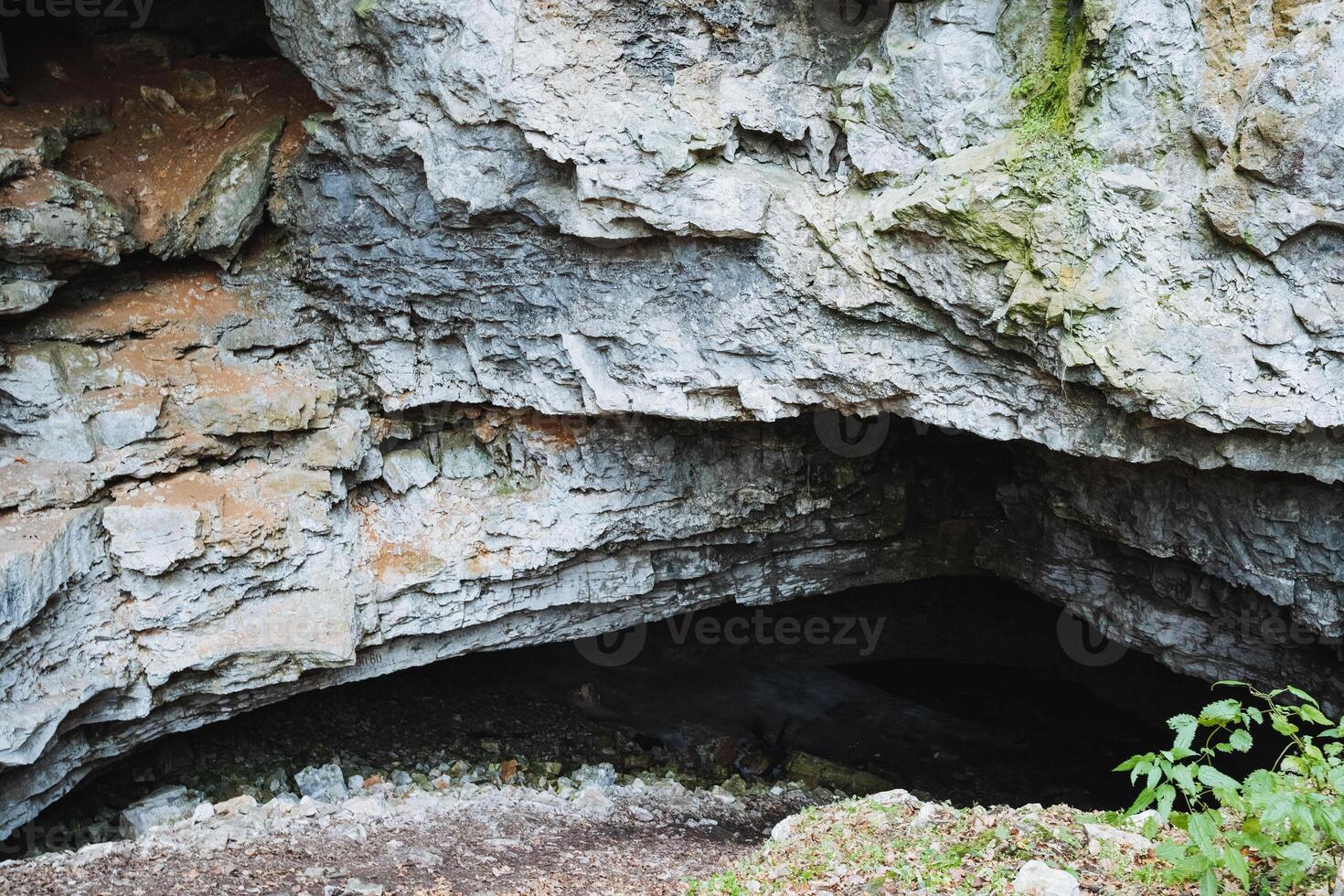 Deep within the steep cliffside lies a small, mysterious cave that formed over countless years through the relentless processes of natures erosion and various geological forces at work photo
