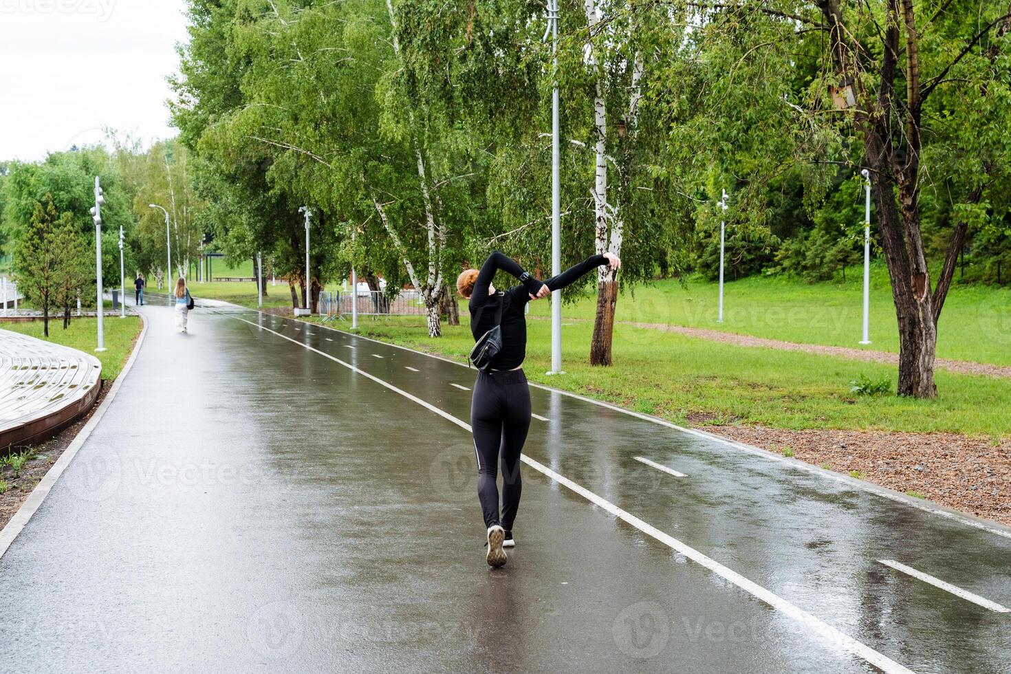 A dedicated young woman exercises in a deserted park on a rainy running path, showing focus on her fitness routine and wellbeing. She is athletic and committed to her workout photo