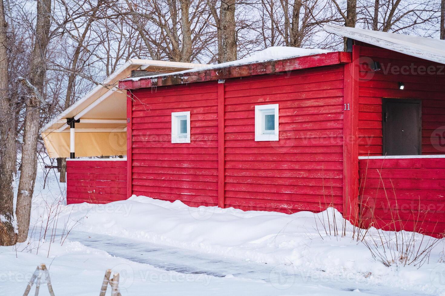 In a picturesque winter landscape, a charming red house stands proudly, enveloped by a blanket of snow and surrounded by tall, majestic trees that add to its serene beauty photo