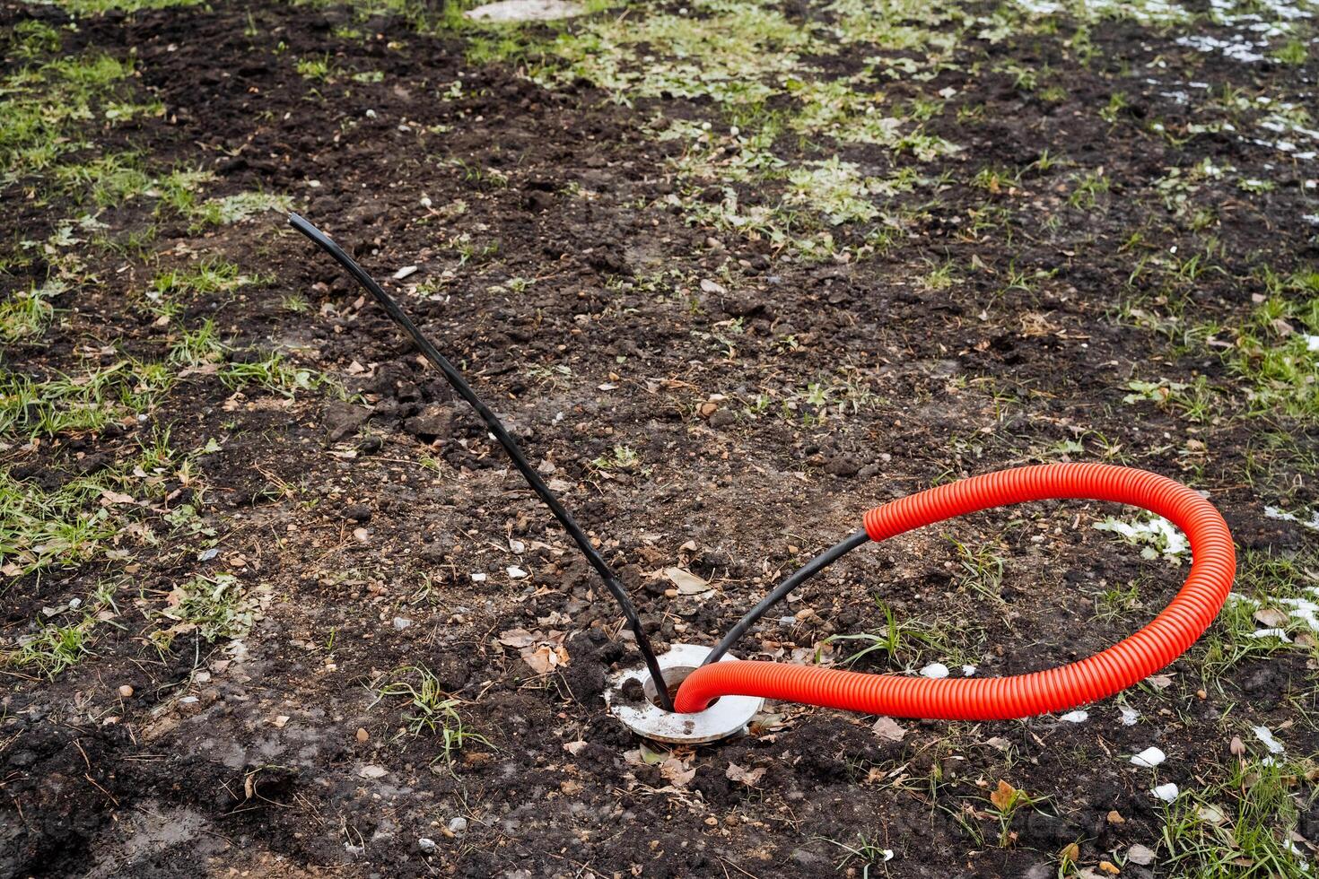 A bright red rubber ring is currently resting and laying in the dirt, partially buried in the ground, surrounded by various natural elements of the environment all around it photo
