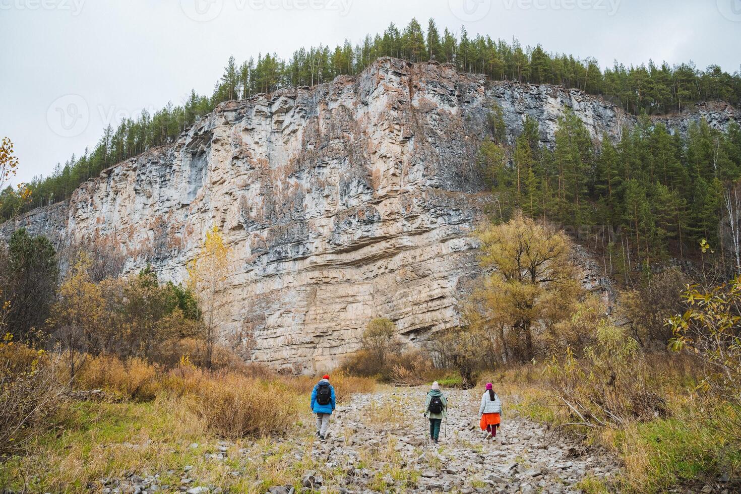 Two individuals casually stroll along a rugged and uneven path that lies in front of a grand mountain, taking a moment to pause and savor the breathtaking beauty of nature surrounding them photo