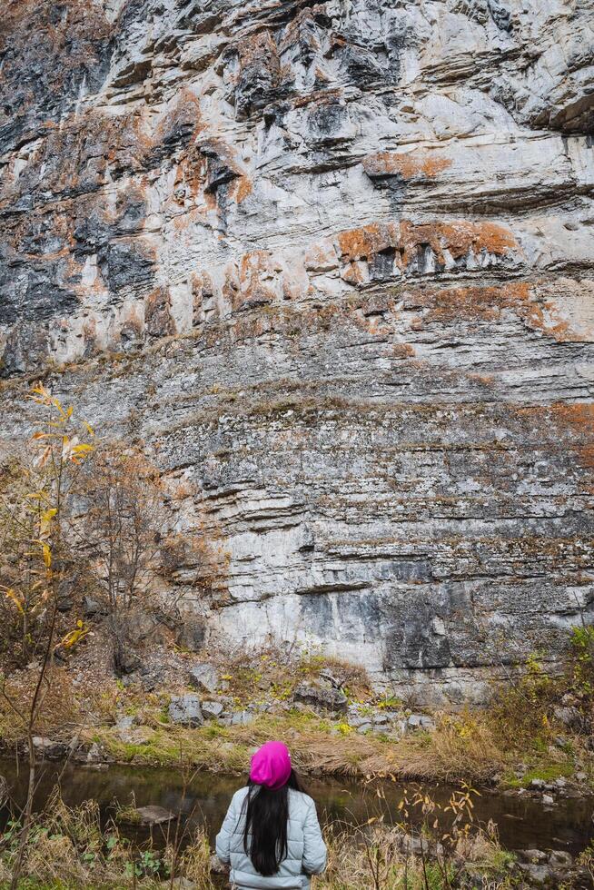 A hiker is admiring the breathtaking and majestic rocky cliffs while exploring the stunning autumn forest during their adventure in nature photo
