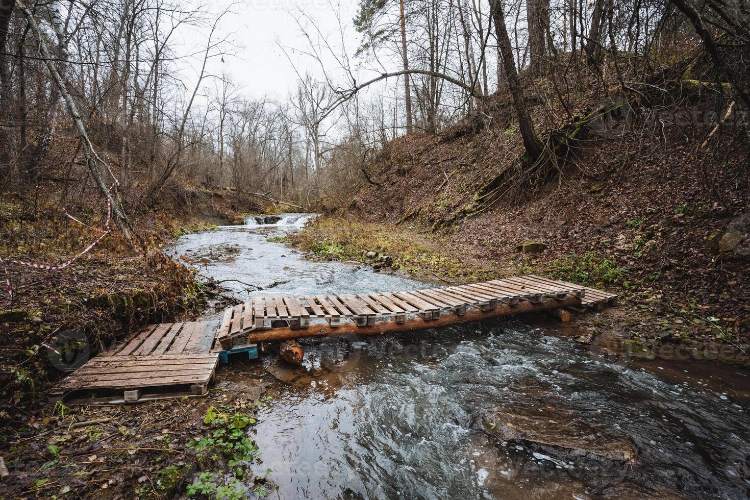 A charming wooden bridge gracefully spans over a tranquil river that meanders through the serene woods, surrounded by lush greenery and tall trees that create a picturesque landscape photo
