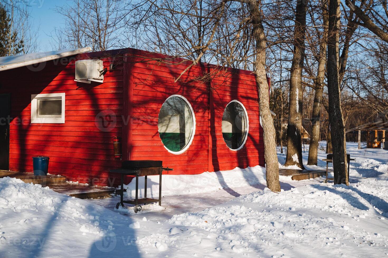A vibrant red house with charming round windows contrasts beautifully with fluffy white snow, creating a picturesque winter scene that captivates the eye and sparks imagination photo