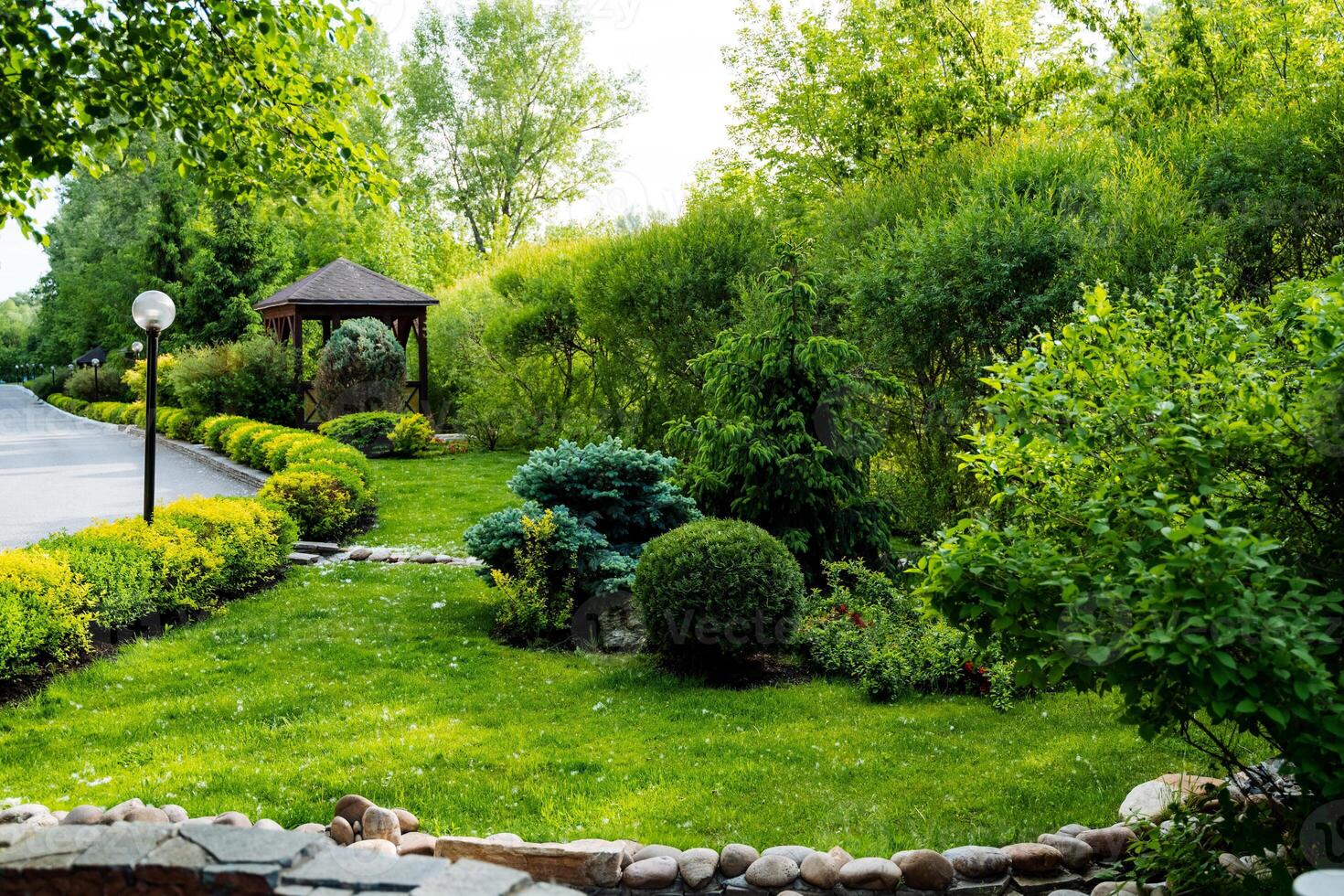 The garden is enchanting with its abundant greenery, stone wall, and charming gazebo, offering a peaceful and inviting outdoor space to unwind and appreciate natures beauty photo