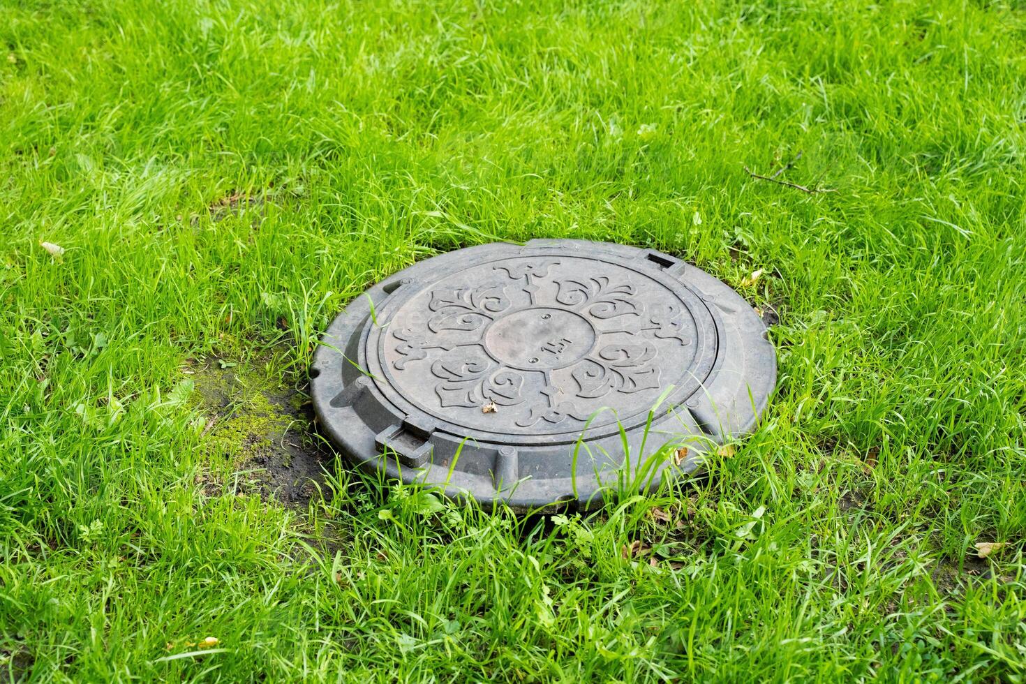 In the center of a beautifully lush green field, a manhole cover is situated, contrasting with the surrounding vibrant grass and landscape, creating a unique focal point in the garden photo