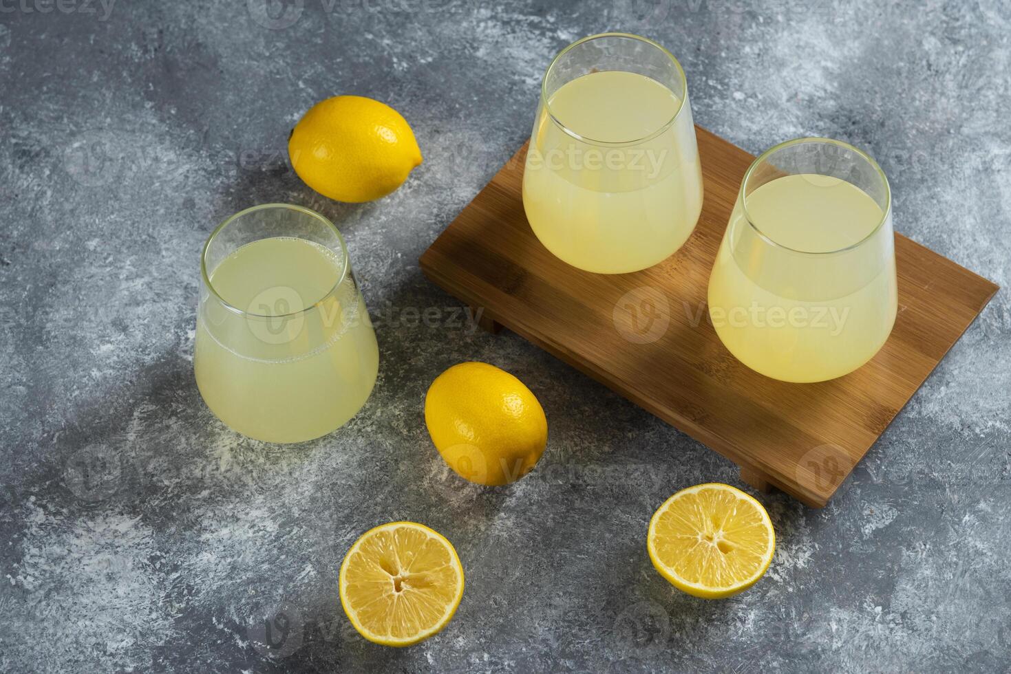 Three glass cups with fresh lemon juice on a wooden board photo