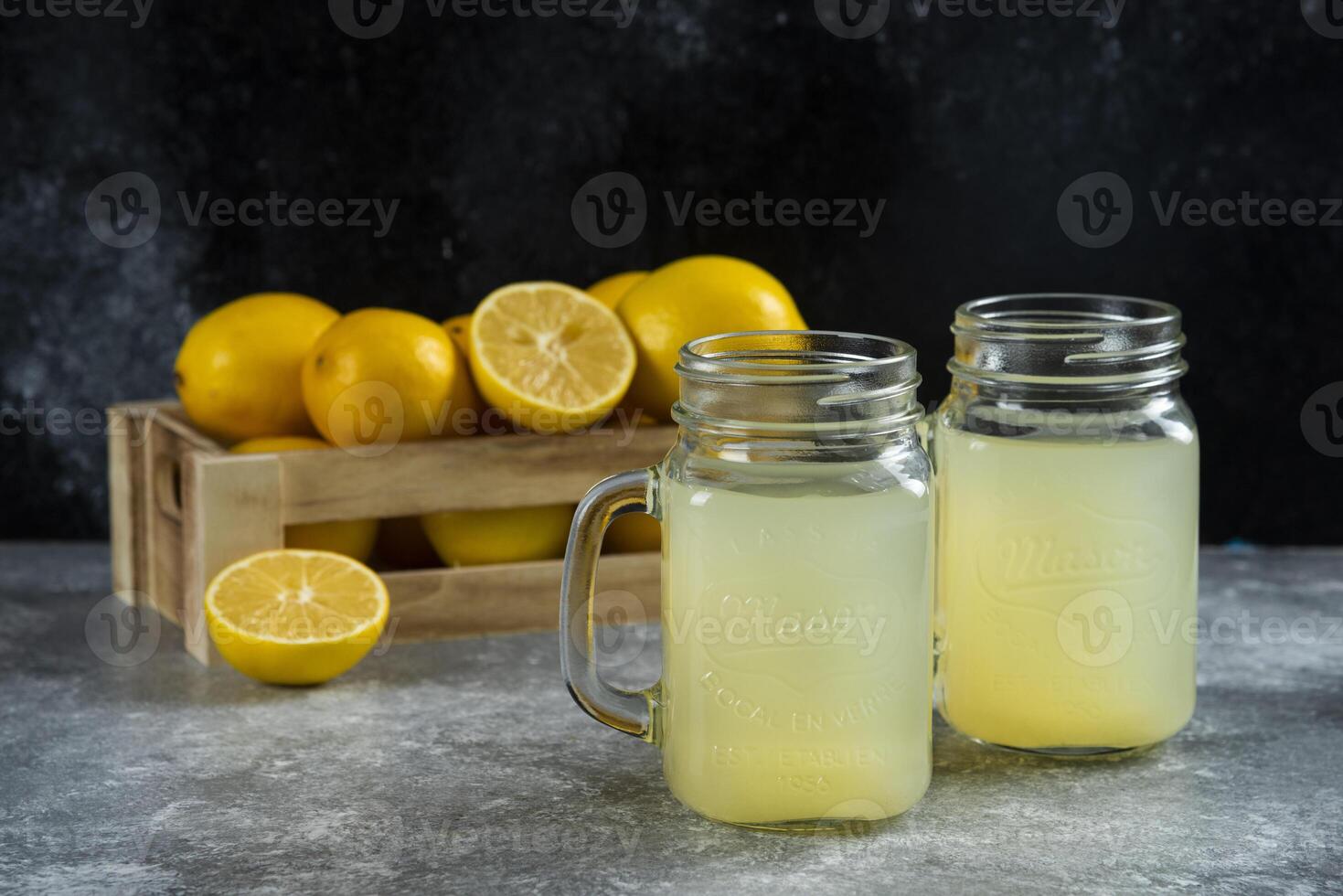 Two glass jars of delicious lemon juice and slices on a marble background photo