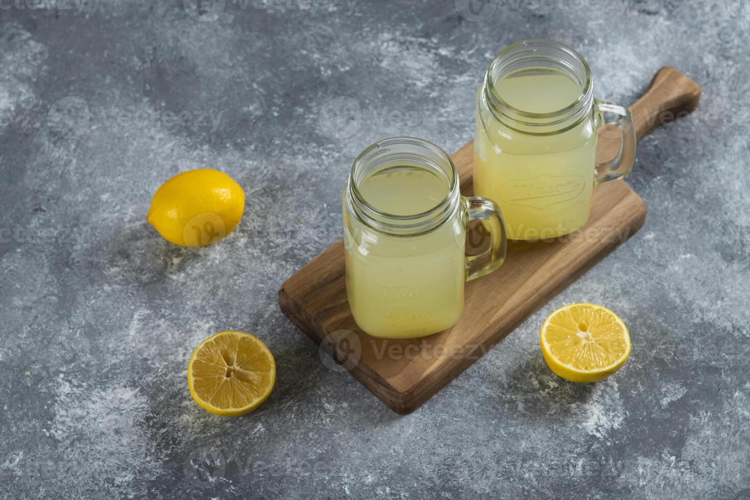 Two glass jars of lemon juice and slices on a wooden board photo