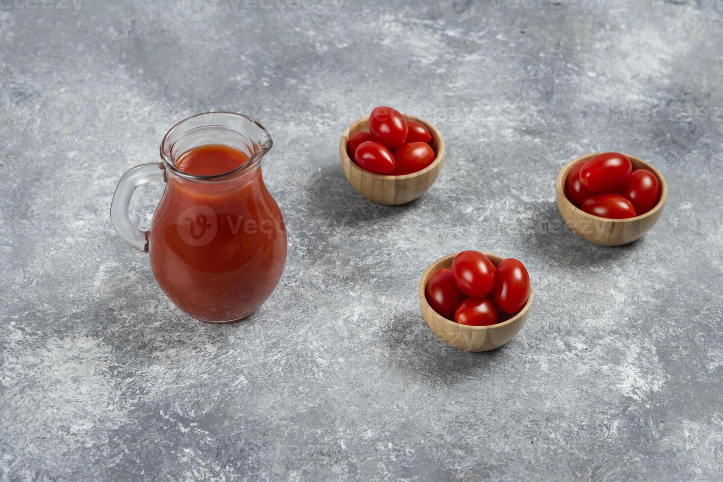 A glass pitcher full of tomato juice with wooden bowls of cherry tomato photo