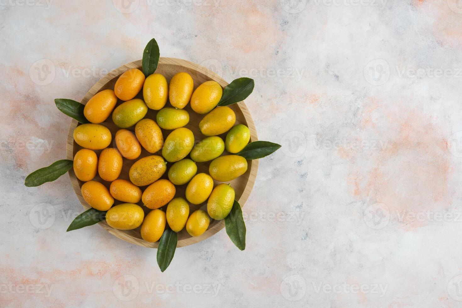 Top view of kumquats and leaves on wooden plate photo