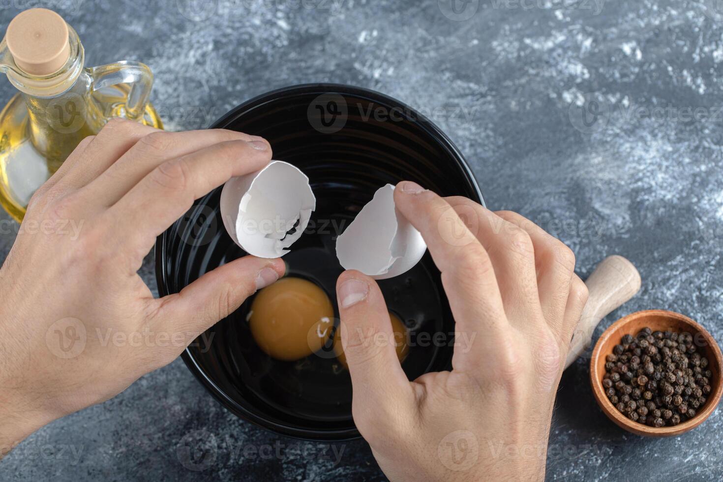 Male hands breaking eggs in black bowl photo