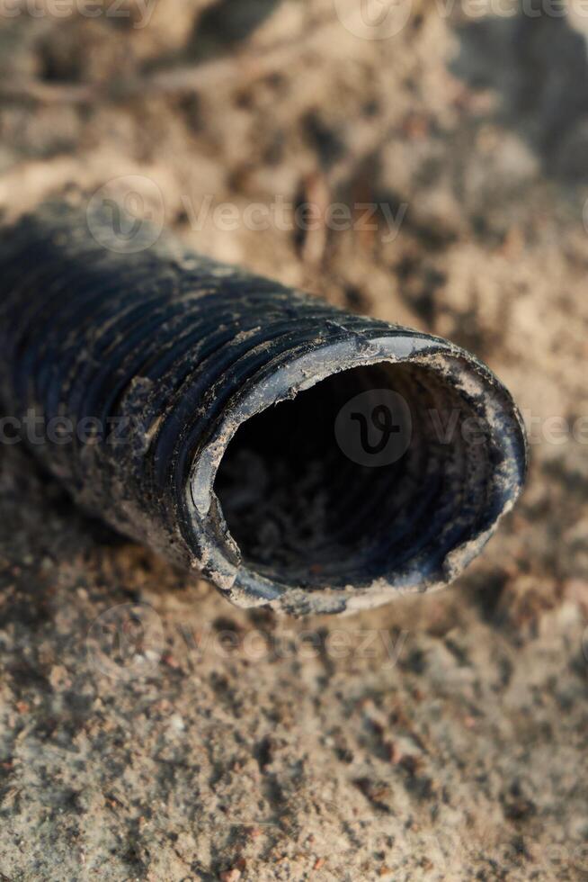 A CloseUp View of a Weathered and Aged Pipe Sitting on Sandy Ground with Surroundings photo