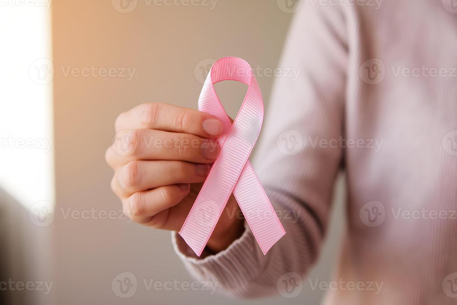 Pink ribbon held gently, symbolizing awareness and support in softly lit scene photo